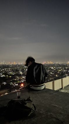 a man sitting on top of a roof looking at the city lights in the distance