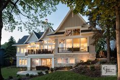 a large house with lots of windows and lights on it's front porch, surrounded by trees