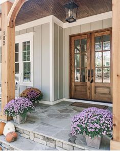 the front porch is decorated with purple flowers and potted plants, along with two pumpkins