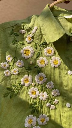 a green shirt with white daisies on the front and yellow flowers on the back