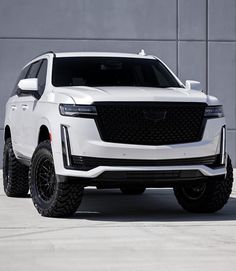 a white suv is parked in front of a gray wall with black wheels and tires