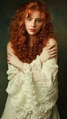 a woman with long red hair is posing for a photo wearing a white dress and holding her arms on her chest