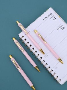 three pink and gold pens sitting next to each other on top of a notepad