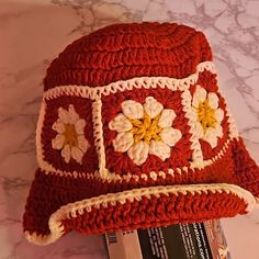 a red crocheted hat sitting on top of a white marble counter next to a magazine