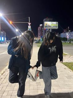 two people walking down the sidewalk at night with their hands in each other's pockets