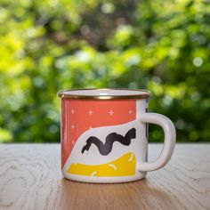 a coffee cup sitting on top of a wooden table next to a forest filled with trees