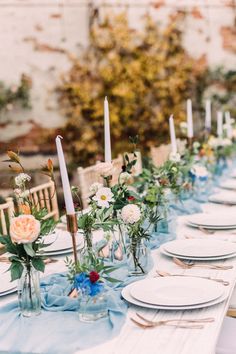 a long table with white plates and blue napkins is set for an outdoor dinner