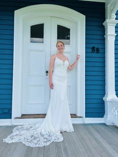 a woman standing in front of a blue house wearing a wedding dress and holding her hand out