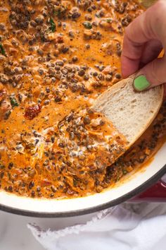 a person dipping a piece of bread into a pot of chili soup with cheese on top