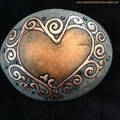 a heart shaped metal object sitting on top of a black surface with swirly designs