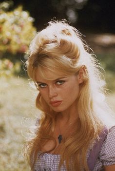 a woman with long blonde hair and blue eyes posing for a photo in the grass