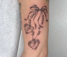 a woman's arm with a tattoo on it that has hearts and pearls attached to the wrist