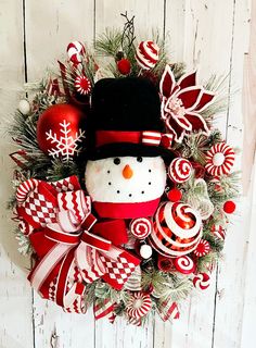 a snowman wreath with candy canes and ornaments around it on a white wooden wall