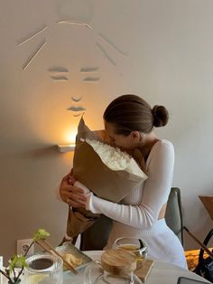 a woman holding a brown paper bag over her face while sitting at a table with food on it