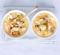 two bowls of soup with shrimp and scallops on a blue towel next to a spoon