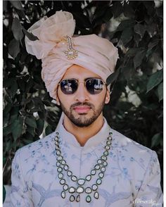 a man wearing sunglasses and a turban standing in front of a tree with leaves