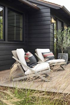 two lawn chairs sitting on top of a wooden deck in front of a black house