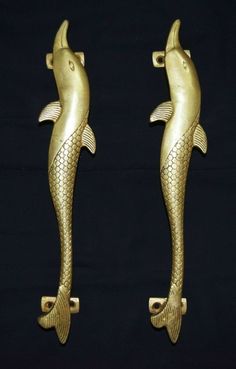 two gold colored fish shaped door handles on black background