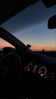 the dashboard of a car at dusk with the sun setting in the distance behind it