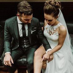 a bride and groom are sitting on a bench in front of a black leather couch