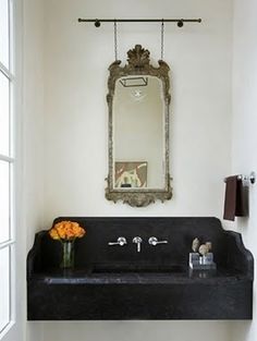 a bathroom sink sitting under a mirror next to a window with flowers on the counter