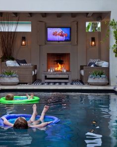 two people floating on inflatable rafts in a pool with a tv and fire place