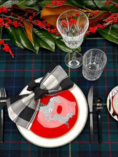 the table is set with red and black plates, silverware, and plaid napkins