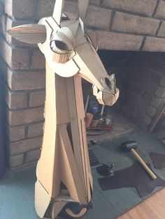 a horse made out of cardboard sitting in front of a fire place with tools on the floor