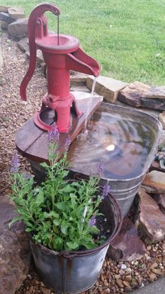 an old fashioned water pump is next to a potted plant with purple flowers in it