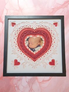 a baby's photo in a heart shaped frame on a pink marble background with black border