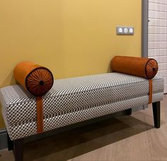 a bench with two pillows on it in front of a yellow wall