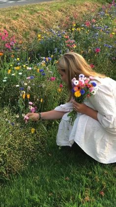 a woman kneeling down in the grass picking flowers