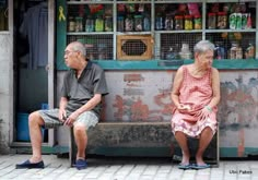 an older couple sitting on a bench in front of a store