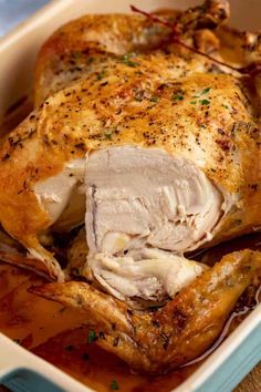 a roasted chicken in a casserole dish with brown gravy on the side