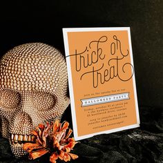 an orange and black halloween party card with a skull on it next to a flower