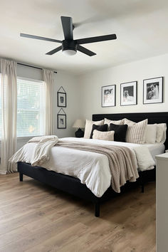 a bedroom with white walls and wood flooring has a black headboard on the bed