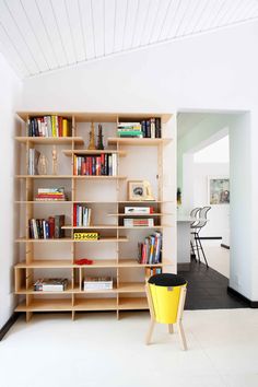 a bookshelf filled with lots of books next to a yellow trash can in a room