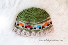 a crocheted green hat with multicolored animals on it sitting on white fur