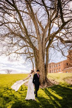 a bride and groom walking in front of a large tree on their wedding day at the farm