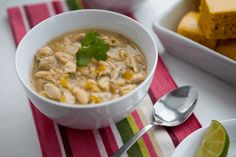 a white bowl filled with soup next to a plate of cornbreads on a table