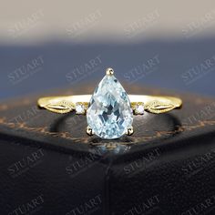 a pear shaped blue topazte and diamond ring sits on a black leather box