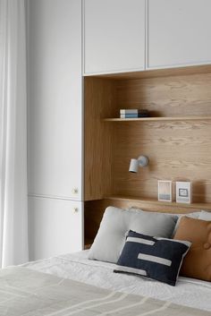 a bed with white sheets and wooden headboard next to a wall mounted bookcase