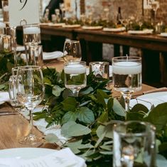 the table is set with wine glasses, candles and greenery for an elegant dinner