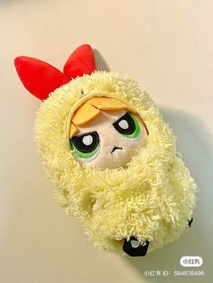 a stuffed animal with green eyes and a yellow coat on it's head, sitting against a white wall