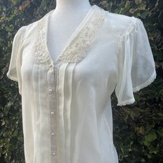 "Dainty Jessica McClintock light and breezy blouse with beautiful lace detail.  Features a split scalloped sleeve trimmed in lace at the hem and shoulder that falls gracefully over the upper arm.  An elegant scalloped embroidered lace collar graces the neck.  Faux pearl buttons grace the front adorned by 2 pleats trimmed in lace on either side.  The cotton is light and breezy and is sure to be a wardrobe favorite. Circa:  1970's Designer:  Gunnies, Jessica's Gunnies of San Francisco Size:  Best V-neck Blouse With Lace Trim For Daywear, Short Sleeve Lace Top For Spring Formal, Formal Short Sleeve Lace Top For Spring, Formal V-neck Tops With Lace Trim, Formal Short Sleeve Lace Top, Vintage Blouse With Lace Sleeves, Spring Vintage Lace Top With Lace Trim, Vintage White Tops With Lace Trim For Daywear, Vintage Tops With Lace Sleeves For Summer