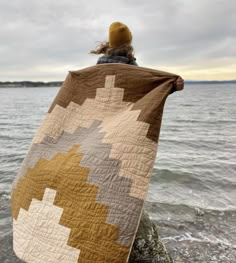 a woman is sitting on the rocks by the water with her blanket draped over her head