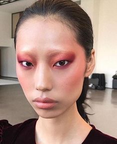 a woman with red makeup and pink eyeshadow is posing for the camera in an empty room