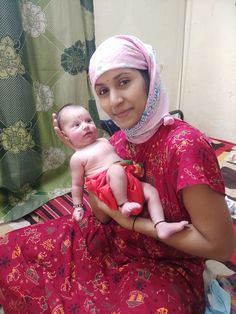 a woman holding a baby wearing a pink head scarf on top of a bed next to a shower curtain