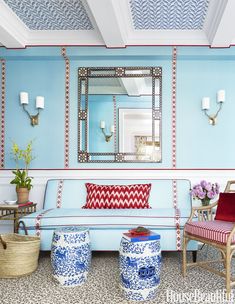 a living room with blue walls and red pillows on the couch, two chairs and a mirror