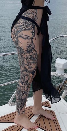 a woman standing on top of a boat next to the ocean with her leg covered in tattoos